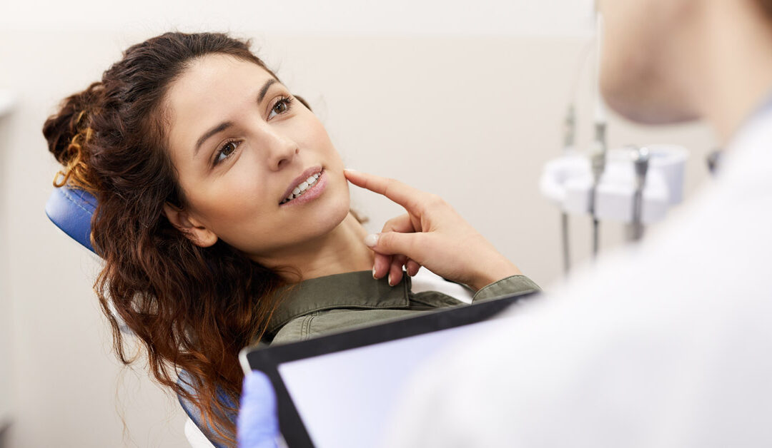 Mujer señalando una parte de la boca a un dentista en la consulta. Esta imagen se utiliza para ilustrar una entrada sobre qué hacer si se te mueve un diente.