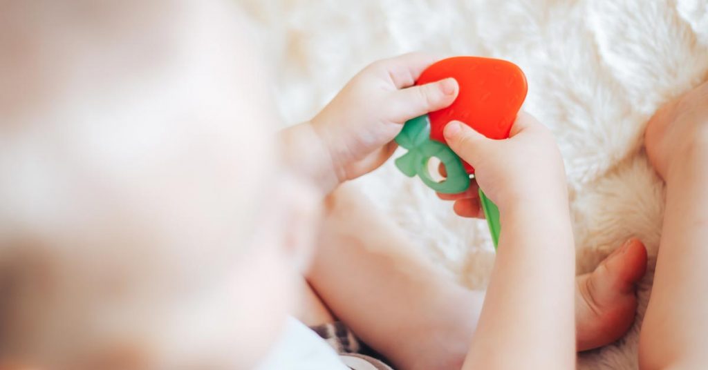 Bebé sentado con un mordedor en la mano que tiene forma de fresa.